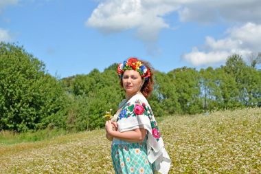 Kafasına bir çelenk ve çiçek açması buğday alan arka planı için bir şans renkli bir eşarp ile olgun kadın