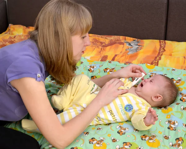La mujer joven lleva la temperatura al bebé enfermo que llora el termómetro electrónico —  Fotos de Stock