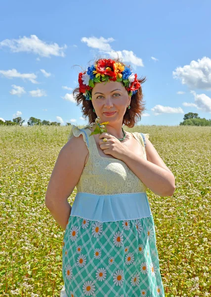 Olgun kadın ile kafasına bir çelenk çiçek buğday alan arka planı tutar.