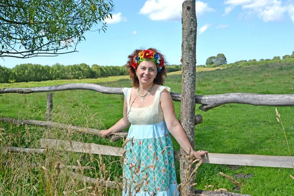 The cheerful woman with a wreath on the head stands near a fence — Stock Photo, Image