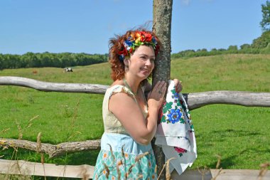 Bir çelenk bir çit ayakta eller güler, renkli bir eşarp ve baştan kadınla