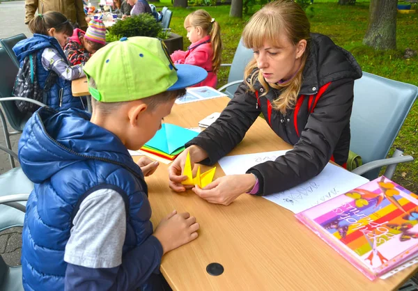 KALINININGRAD, RUSIA - 17 DE SEPTIEMBRE DE 2017: La maestra enseña al niño a poner origami. Clase magistral para niños al aire libre —  Fotos de Stock