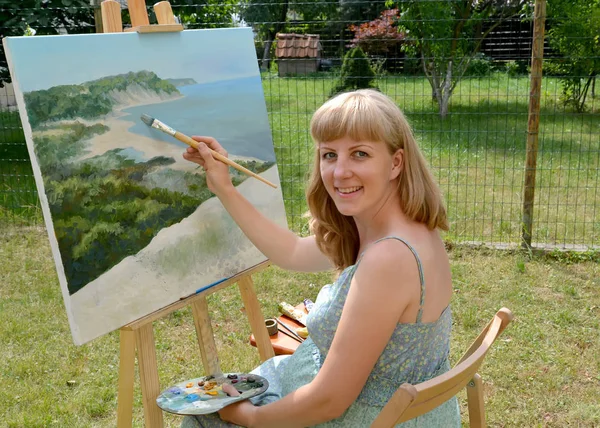 The young pregnant female artist writes a landscape, sitting at an easel — Stock Photo, Image