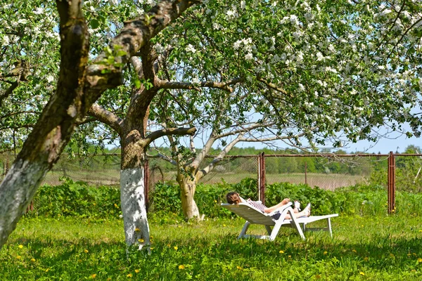 Kadının bir tahta yatakta çiçek açması elma ağacı bahçede bir dinlenme var. Bahar — Stok fotoğraf