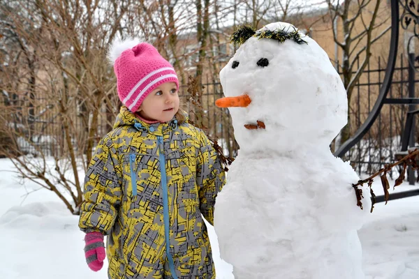 Το κοριτσάκι κοιτάζει έναν χιονάνθρωπο — Φωτογραφία Αρχείου