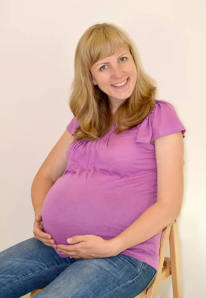 Die junge schwangere Frau umarmt die hände einen bauch auf dem hellen bac — Stockfoto