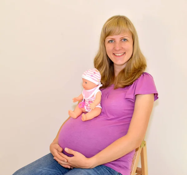 Die junge schwangere Frau hält eine Puppe auf dem Bauch — Stockfoto