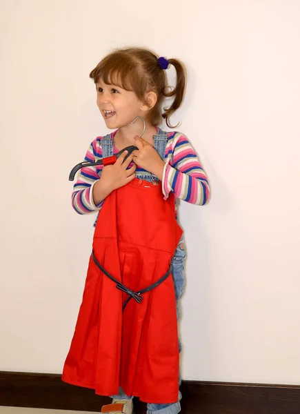 Das kleine fröhliche Mädchen probiert ein schönes rotes Kleid an — Stockfoto