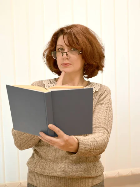 La mujer que lleva gafas y el libro en una mano cuidadosamente mira hacia adelante — Foto de Stock