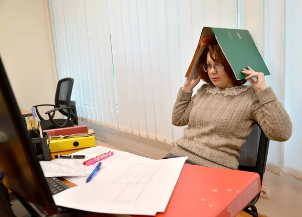 Жінка з жахом дивиться на монітор, тримаючи папку з документами на голові — стокове фото