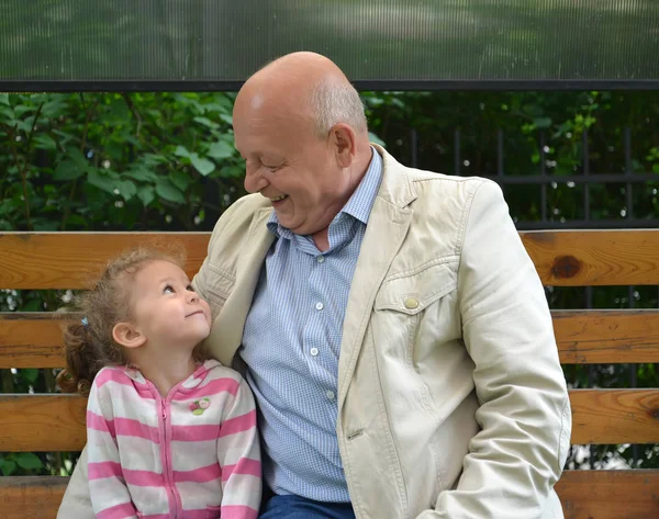 El anciano y la niña con una sonrisa se miran — Foto de Stock