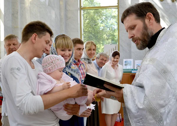 KALINININGRAD, RUSIA - 04 DE AGOSTO DE 2013: Un sacerdote ortodoxo lee una oración y limpia el aceite sagrado de la pierna de un niño después de la unción. Rito de bautismo —  Fotos de Stock