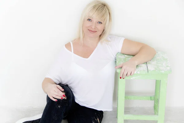 Blond kobieta o niebieskich oczach, siedząc na podłodze w pustym pokoju — Zdjęcie stockowe