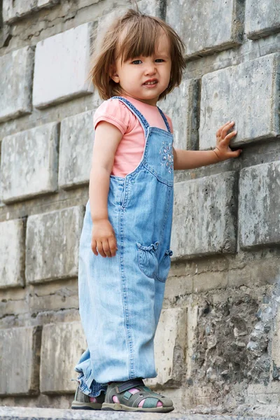 Baby girl in blue cloth standing near wall — Stock Photo, Image