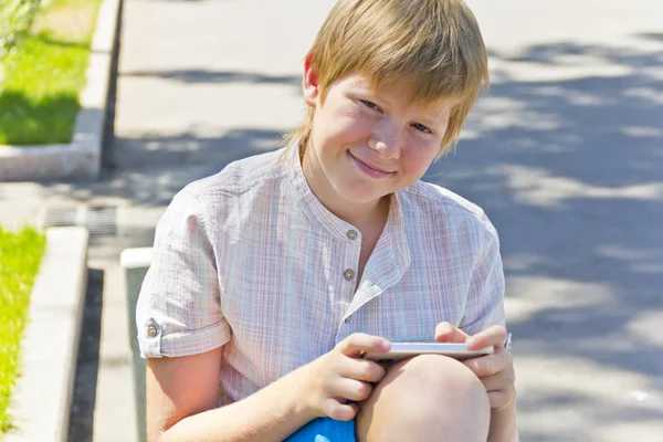 Garçon blond avec téléphone portable assis sur un banc — Photo