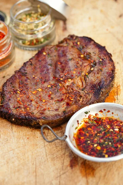 Cooked beef steak with sauces and species on wooden background