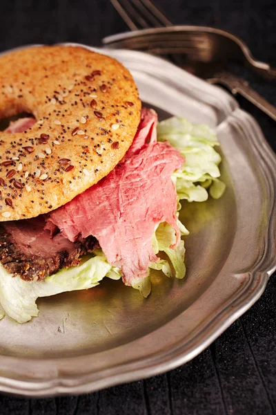 Close up of seeded bagel with steak on tin plate