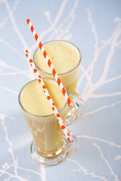 Golden milk turmeric latte in glass with striped straws lying on top on abstract background