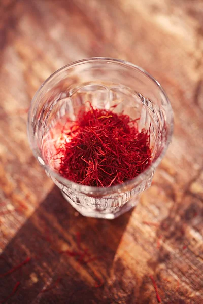 Saffron threads in clear glass, with vintage wood backdrop — ストック写真