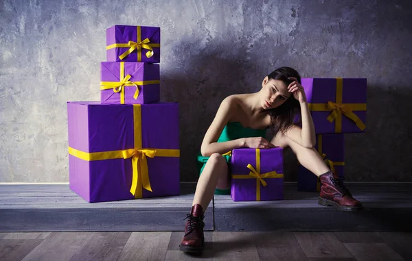 Una giovane ragazza in un vestito e scarpe con un regalo in mano, si siede — Foto Stock