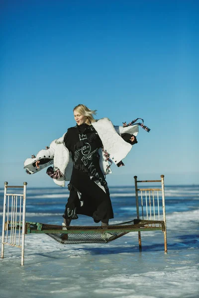 Girl in old clothes jumping on a bed on ice of frozen sea — Stock Photo, Image