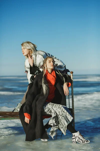 Girls in old clothes are sitting on a bed on the ice of a frozen — Stock Photo, Image