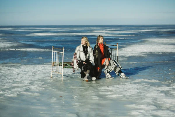Girls in old clothes are sitting on a bed on the ice of a frozen — Stock Photo, Image