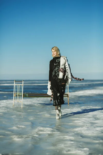 A girl in old clothes walks on ice against the frozen sea and an — Stock Photo, Image