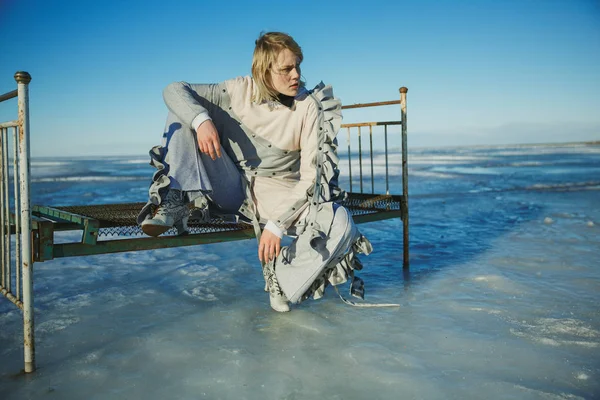 A girl in stylish clothes is sitting on an old bed; Against a fr — Stock Photo, Image