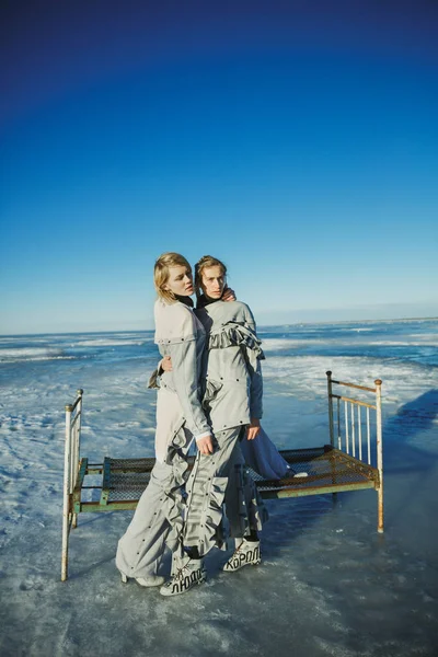 Fashionable girls in stylish clothes stand near an old bed; Agai — Stock Photo, Image