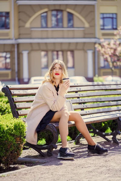 Jeune fille avec une tasse de café assis sur un banc, un s ensoleillé — Photo