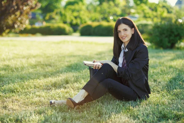 Business woman sitting on grass in sunny park with mobile phone — Stock Photo, Image