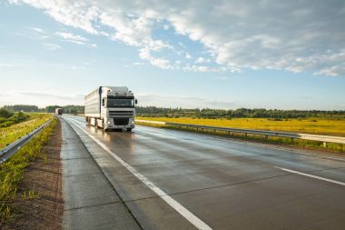Mavi gökyüzüne karşı büyük bir kamyon ile ıslak asfalt yol