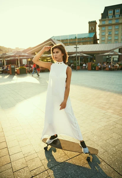 Fille dans une robe blanche et avec un longboard sur la place ensoleillée o — Photo