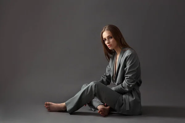 Eine Frau im grauen Pyjama sitzt auf einem grauen Hintergrund — Stockfoto