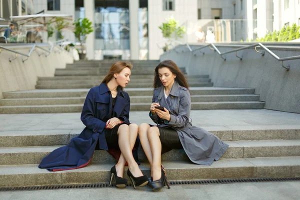 Due donne d'affari in cappotti stanno negoziando sullo sfondo di — Foto Stock