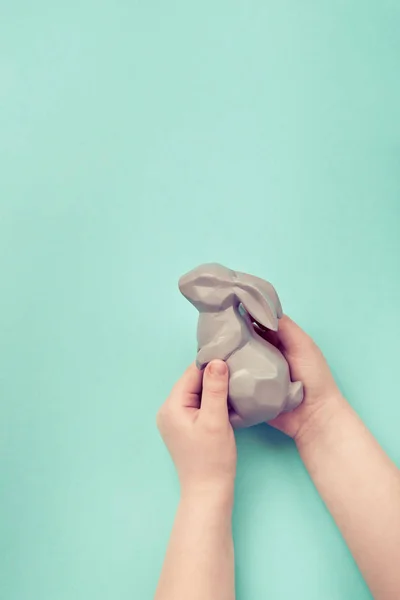 As mãos de criança que mantêm uma estatueta de coelho de Páscoa, apartamento põem-se no azul — Fotografia de Stock