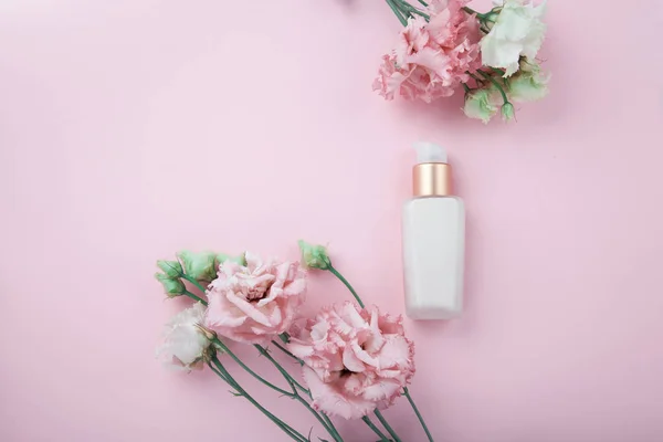 Gezichtscrème met verse roze en witte bloemen, flatlay op roze — Stockfoto