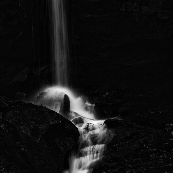 Waterfall in forest landscape long exposure flowing through trees and over rocks in black and white