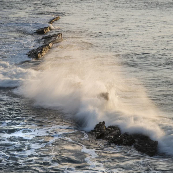 Κύμα συντρίβεται πέρα από τους βράχους στον ωκεανό στην Ανατολή του ηλίου με μακρά έκθεση — Φωτογραφία Αρχείου