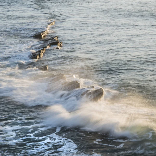 Vague s'écrasant sur les rochers dans l'océan au lever du soleil avec une longue exposition — Photo