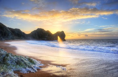 Landscape image of sunrise shining through the arch of Durdle Do clipart