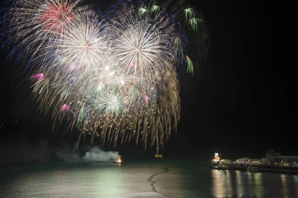 Stunning fireworks display over sea with pier  and boats in wate — Stock Photo, Image