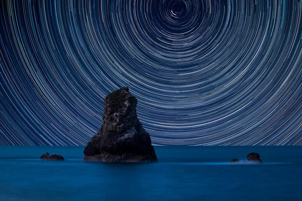 环绕着北极星的星迹的数字合成图像与美丽的长期暴露的大海中岩石的和平景观 — 图库照片