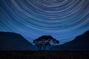 İngiltere 'nin göl bölgesindeki döküntü suyu çevreleyen güzel sisli kırsal manzaralı Polaris etrafındaki yıldız izlerinin dijital kompozit görüntüsü.