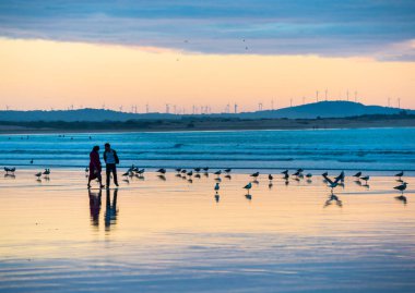 Essaouira, Fas 'ta gün batımında sahilde yürüyen bir çift silueti.