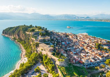 Yunanistan 'ın Nafplio kenti, gün batımında yukarıdan manzaralı küçük evleri olan yeşil yarımada üzerinde