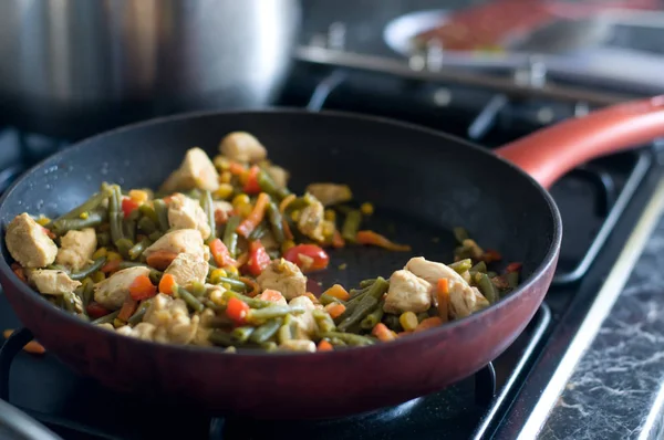 Chicken meat and vegetables cooking in red frying pan — Stock Photo, Image