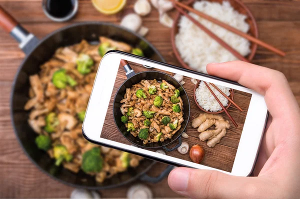 Mãos tirando foto brócolis de frango e cogumelo fritar com smartphone . — Fotografia de Stock