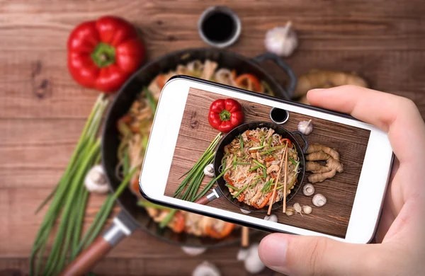 Hands taking photo spicy chicken and veggie noodles with smartphone. — Stock Photo, Image